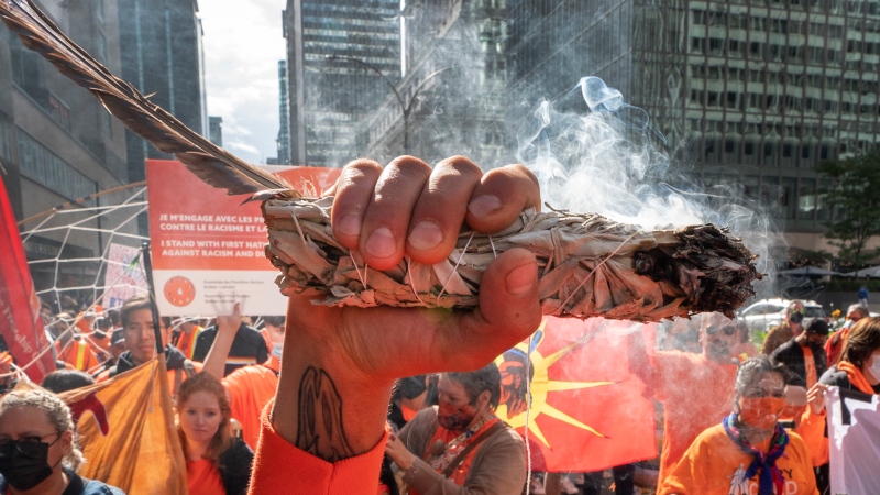 A man holds up an eagle feather and burns sweet grass as people take part in a march to mark the first National Day for Truth and Reconciliation Thursday, September 30, 2021 in Montreal.THE CANADIAN PRESS/Ryan Remiorz
