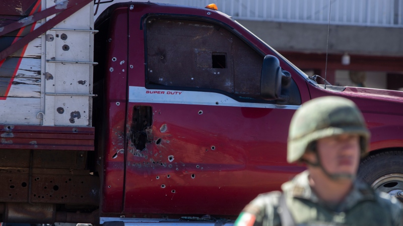 A soldier stands near a bullet ridden truck after a shootout in Parangaricutiro, Mexico,Thursday, March 10, 2022. Authorities in the avocado-growing zone of western Mexico said five suspected drug cartel gunmen were killed in a massive firefight between gangs. The Mexican government filed a lawsuit against U.S. gun manufacturers arguing their commercial practices has led to bloodshed in Mexico. A U.S. judge has dismissed the lawsuit. ( AP Photo/Armando Solis)