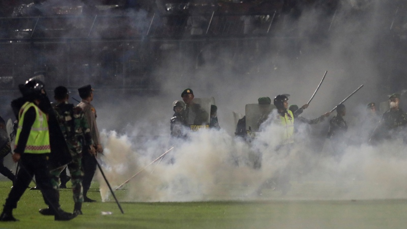 Police officers and soldiers stand amid tear gas smoke during a soccer match at Kanjuruhan Stadium in Malang, East Java, Indonesia, Saturday, Oct. 1, 2022. (AP Photo / Yudha Prabowo)