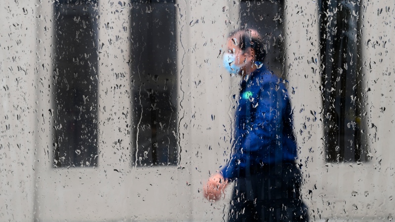 A pedestrian walks alongside businesses on a rainy day while wearing a protective mask during the COVID-19 pandemic in Toronto on Friday, June 18, 2021.(THE CANADIAN PRESS/Nathan Denette) 