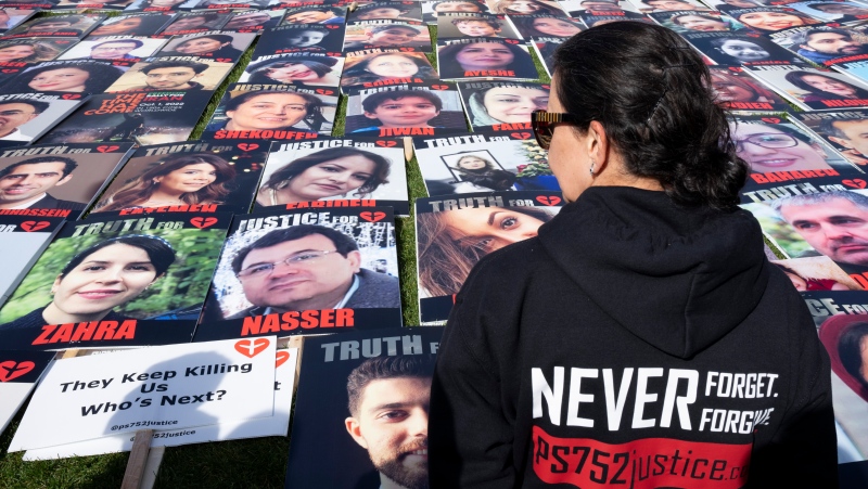 A woman views the photos of people killed on Flight PS752 during a protest against Iran on Parliament Hill, Tuesday, Oct. 4, 2022 in Ottawa. THE CANADIAN PRESS/Adrian Wyld 