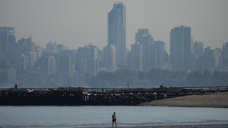 A man walks in the water off Locarno Beach during a stretch of unseasonably warm weather as smoke from wildfires burning in B.C. and in the U.S. hangs over the downtown core, in Vancouver, B.C., Thursday, Oct. 6, 2022. (THE CANADIAN PRESS/Darryl Dyck)
