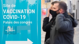 People walk by a COVID-19 vaccination sign at a vaccination site in Montreal, Saturday, Jan. 8, 2022. Federal health officials urged Canadians to wear face masks indoors and continue following other public health precautions during a COVID-19 update on Nov. 10. THE CANADIAN PRESS/Graham Hughes
