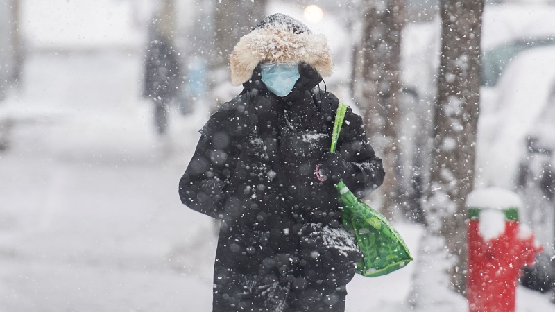 A person wears a face mask as they walk along a street during snowfall in Montreal, Wednesday, November 16, 2022. The Quebec government has recommended wearing masks in public spaces. THE CANADIAN PRESS/Graham Hughes
