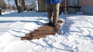 A Winnipegger walking across planks of wood to deal with the snow fall. Nov. 22, 2022. (Source: Josh Crabb/CTV News)