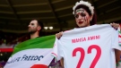 A fan painted her face holds a jersey with the name of Mahsa Amini, a woman who died while in police custody in Iran at the age of 22, ahead of the World Cup group B soccer match between Wales and Iran, at the Ahmad Bin Ali Stadium in Al Rayyan , Qatar, Friday, Nov. 25, 2022. (AP Photo/Pavel Golovkin)