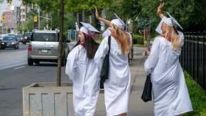Notre Dame High School graduates (left to right) Lauryn Madigan, Meg Botelho and Claire Lackey wave to honking drivers as they celebrate with a walk down a street in Toronto on Monday, June 22, 2020. (THE CANADIAN PRESS/Frank Gunn)