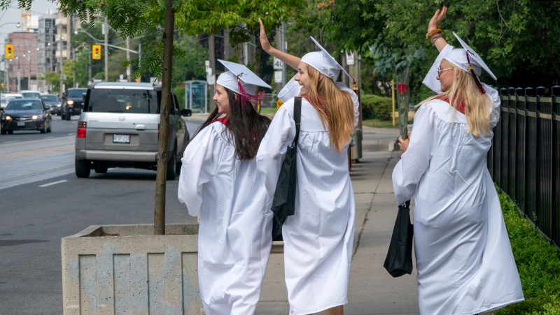 Notre Dame High School graduates (left to right) Lauryn Madigan, Meg Botelho and Claire Lackey wave to honking drivers as they celebrate with a walk down a street in Toronto on Monday, June 22, 2020. (THE CANADIAN PRESS/Frank Gunn)