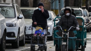 A man smokes while pushing a trolley loaded with groceries on a quiet street in Beijing, China, on Nov. 29, 2022. (Andy Wong / AP) 