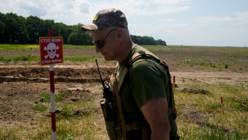 A Ukrainian soldier walks near a post warning about landmines in a field on the outskirts of Kyiv, Ukraine, Thursday, June 9, 2022. (AP Photo/Natacha Pisarenko)