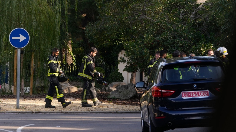 Firefighters walk past a diplomatic car by the Ukrainian embassy in Madrid, Spain, Wednesday, Nov. 30, 2022. (AP Photo/Paul White)