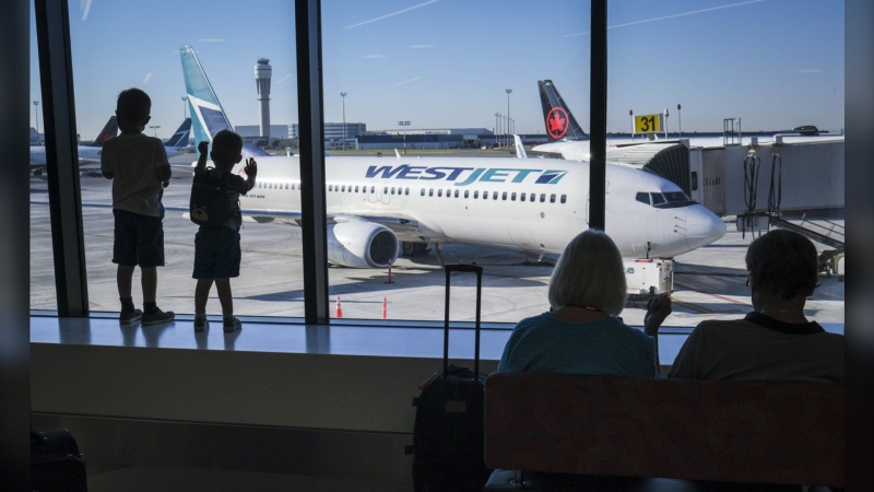 Young boys look out at Air Canada and WestJet planes at Calgary International Airport in Calgary, Alta., Wednesday, Aug. 31, 2022. WestJet announces its first flight to Asia in a plan to expand Calgary's airport capacity by over 25 per cent by next year. (THE CANADIAN PRESS/Jeff McIntosh)