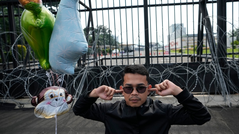An activist plugs his ears during a protest in front of the parliament building in Jakarta, Indonesia, Tuesday, Dec. 6, 2022. Indonesia's Parliament passed a long-awaited and controversial revision of its penal code Tuesday that criminalizes extramarital sex for citizens and visiting foreigners alike. (AP Photo/Achmad Ibrahim) 