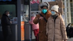 A couple wearing face masks walk past residents get their routine COVID-19 throat swabs at a coronavirus testing site in Beijing, Wednesday, Dec. 7, 2022. China has announced new measures rolling back COVID-19 restrictions, including limiting lockdowns and testing requirements. (AP Photo/Andy Wong)