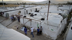 Syrian refugees walk by their tents at a refugee camp in the town of Bar Elias, in the Bekaa Valley, Lebanon, July 7, 2022. A funding shortfall for fragile Middle Eastern states who host refugees could lead to turbulence in international relations, warns the UN refugee chief for that region. (THE CANADIAN PRESS/AP-Bilal Hussein)