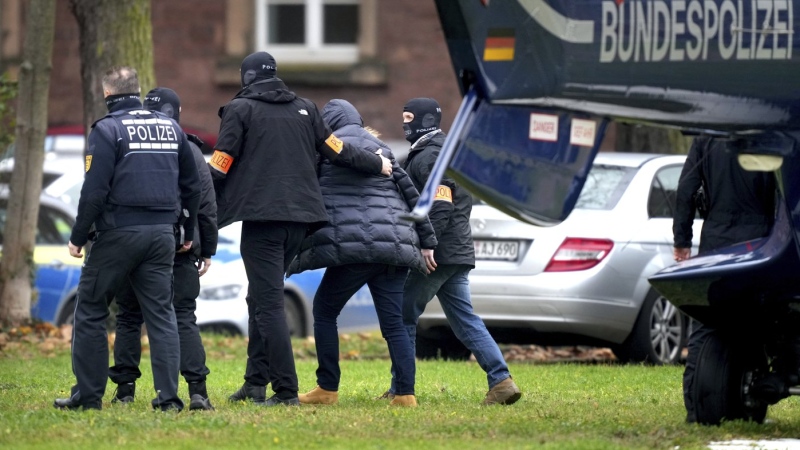 An suspect, second right, is escorted from a police helicopter by police officers after the arrival in Karlsruhe, Germany, Wednesday, Dec. 7, 2022. Thousands of police officers carried out raids across much of Germany on Wednesday against suspected far-right extremists who allegedly sought to overthrow the government in an armed coup. Officials said 25 people were detained. (AP Photo/Michael Probst)