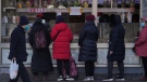 A resident wearing a face mask walks by women who line up to buy snack foods at a store in Beijing, Tuesday, Jan. 17, 2023. (AP Photo/Andy Wong)