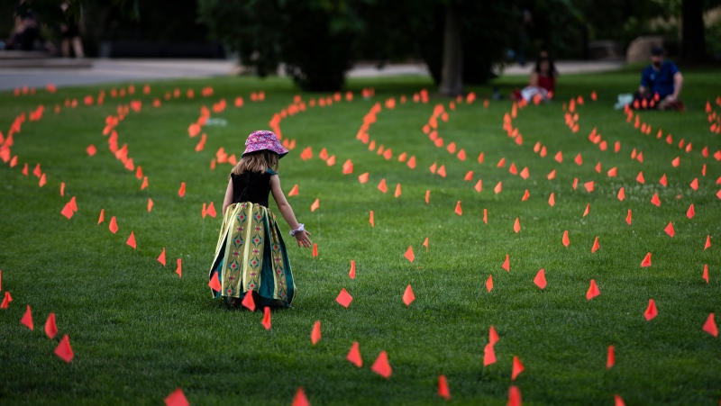 Margot King, 4, touches an orange flag, representing children who died while attending Indian Residential Schools in Canada, placed in the grass at Major's Hill Park in Ottawa, on Canada Day, Thursday, July 1, 2021. (THE CANADIAN PRESS/Justin Tang)