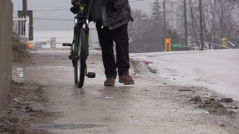 A homeless man walks along the sidewalk with a bike in the east end of Barrie, Ont. (CTV News/Mike Arsalides)