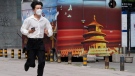 A man wearing a mask runs near a propaganda poster in Beijing, China, on July 16, 2022. (Ng Han Guan / AP)