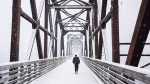 A man walks across a pedestrian bridge during a snow storm in Fredericton on Sunday, December 27, 2015. THE CANADIAN PRESS/Darren Calabrese 