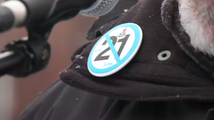 A speaker wears an anti-Bill 21 pin at a Montreal commemoration on Jan. 27, 2023 for victims of the 2017 Quebec City mosque shooting. (CTV News/Kelly Greig) 