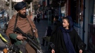 A Taliban fighter stands guard as a woman walks past in Kabul, Afghanistan, Monday, Dec. 26, 2022.