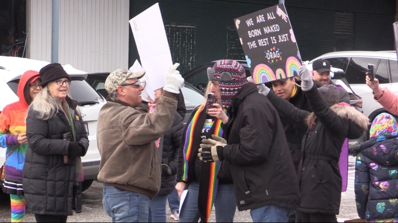 A protester holding a sign is surrounded by supporters of drag queen story time at a rally in Sarnia, Ont. on Jan. 28, 2023 (Brent Lale/CTV News London)