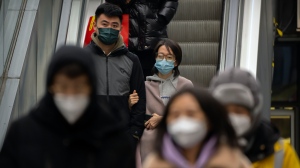 People wearing face masks ride an escalator at a shopping and office complex in Beijing, on Jan. 11, 2023. (AP Photo/Mark Schiefelbein)