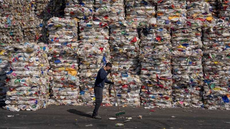 A GreenNet recycling plant employee cleans the ground next to piles of disposable plastic ready for export, in Atarot industrial zone, north of Jerusalem, Jan. 25, 2023. (AP Photo/Oded Balilty)