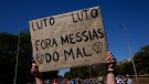 An activist carries a sign written in Portuguese that reads 'Mourning, Mourning, out Evil Messiah,' in reference to Brazil's President Jair Messias Bolsonaro, during a rally demanding authorities conduct a thorough investigation into the circumstances leading to their deaths, and do more to protect indigenous lands against illegal miners, loggers, and fishermen, in Brasilia, Brazil, Sunday, June 19, 2022. (AP Photo/Eraldo Peres)