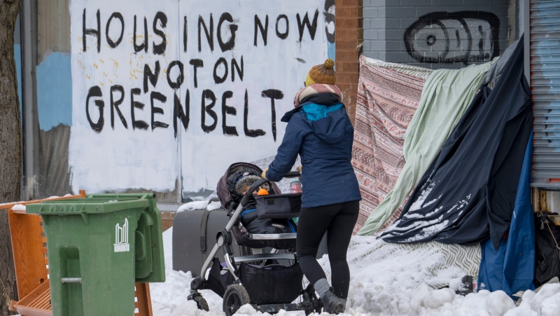 A woman pushes a stroller past the shelter of an unhoused person in Toronto on Tuesday January 31, 2023 as the coldest weather in years arrives. THE CANADIAN PRESS/Frank Gunn