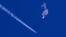 In this photo provided by Chad Fish, the remnants of a large balloon drift above the Atlantic Ocean, just off the coast of South Carolina, with a fighter jet and its contrail seen below it, Saturday, Feb. 4, 2023. (Chad Fish via AP) 