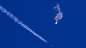 In this photo provided by Chad Fish, the remnants of a large balloon drift above the Atlantic Ocean, just off the coast of South Carolina, with a fighter jet and its contrail seen below it, Saturday, Feb. 4, 2023. (Chad Fish via AP) 