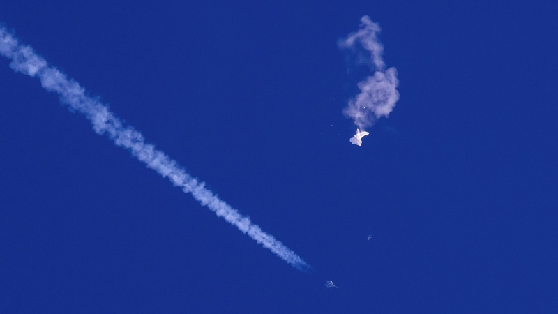 In this photo provided by Chad Fish, the remnants of a large balloon drift above the Atlantic Ocean, just off the coast of South Carolina, with a fighter jet and its contrail seen below it, Feb. 4, 2023.  (Chad Fish via AP, File) 