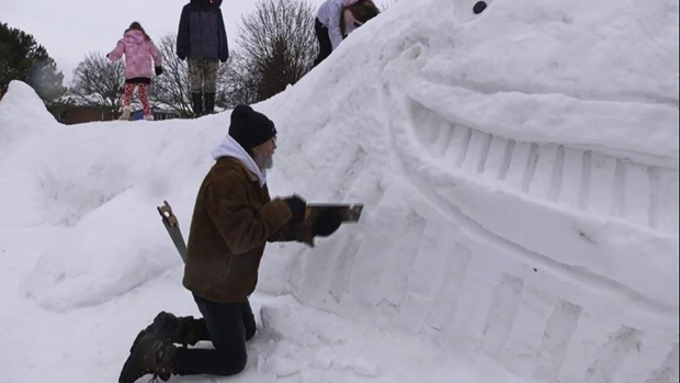 Ken Weichel, of Innisfil, Ont., carves a whale out of snow on his front yard on Tues., Feb. 7, 2023, that his grandchildren enjoy to play on. (CTV News/Molly Frommer)