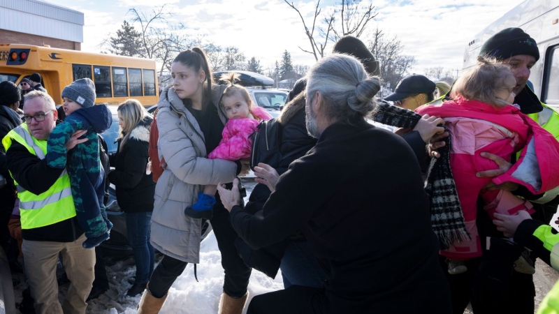 Parents and their children are loaded onto a warming bus as they wait for news after a bus crashed into a daycare centre in Laval, Que., on Wednesday, February 8, 2023. THE CANADIAN PRESS/Ryan Remiorz
