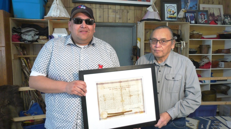 Zongidaya Nelson (left) and his uncle  Terrance Nelson hold a framed copy of the 1875 amendment to a Treaty 1 annual payment agreement with the Government of Canada. (Image source: Taylor Brock/CTV News Winnipeg)