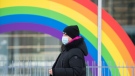 A woman wears a face mask as she walks by a rainbow in Montreal, Saturday, February 6, 2021, as the COVID-19 pandemic continues in Canada and around the world. THE CANADIAN PRESS/Graham Hughes