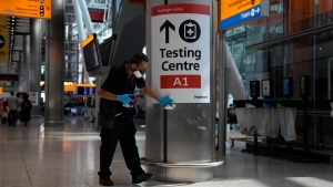 A worker cleans surfaces next to a COVID-19 testing sign as a precaution against coronavirus, at Terminal 5 of Heathrow Airport in London on Aug. 2, 2021. (AP Photo/Matt Dunham)