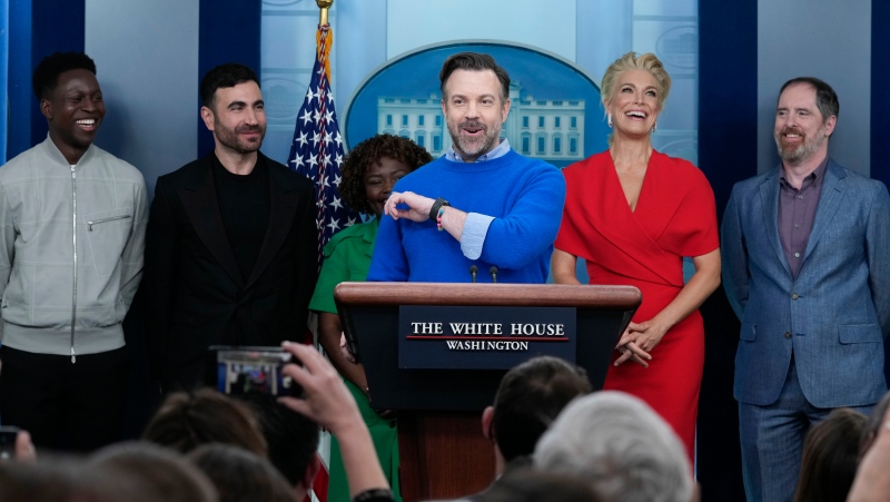 Jason Sudeikis, fourth from left, who plays the title character in the Apple TV+ series “Ted Lasso”, speaks as he joins White House press secretary Karine Jean-Pierre, third from left, and fellow cast members, from left, Toheeb Jimoh, Brett Goldstein, Hannah Waddingham, and Brendan Hunt, during the daily press briefing at the White House in Washington, Monday, March 20, 2023. (AP Photo/Susan Walsh) 