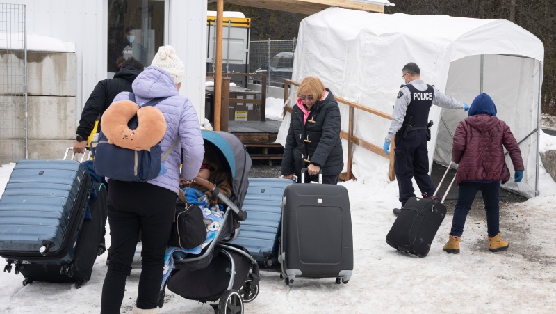 A family of asylum seekers from Colombia is met by an RCMP officer after crossing the border at Roxham Road into Canada, February 9, 2023 in Champlain, New York. THE CANADIAN PRESS/Ryan Remiorz