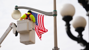 A worker puts up an American flag along Wellington St. in Ottawa on Wednesday, March 22, 2023, in preparation for U.S. President Joe Biden's visit. (Sean Kilpatrick/THE CANADIAN PRESS)