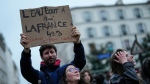 A demonstrator holds a placard that reads, "water boils at 100 degrees celsius, France boils at 49.3, 64 years it's no" during a protest in Paris, Wednesday, March 22, 2023. Macron said Wednesday that the pension bill that he pushed through without a vote in parliament needs to be implemented by the "end of the year." Meanwhile, oil shipments in the country were disrupted amid strikes at several refineries in western and southern France. (AP Photo/Lewis Joly)