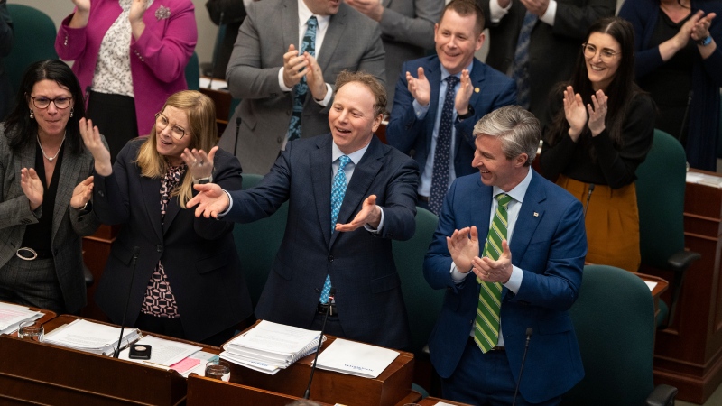 Finance and Treasury Board Minister Allan MacMaster, second from bottom right, standing beside Premier Tim Houston, bottom right, gestures to the opposition parties while tabling the provincial budget at the Nova Scotia legislature in Halifax on Thursday, March 23, 2023. (THE CANADIAN PRESS/Darren Calabrese)