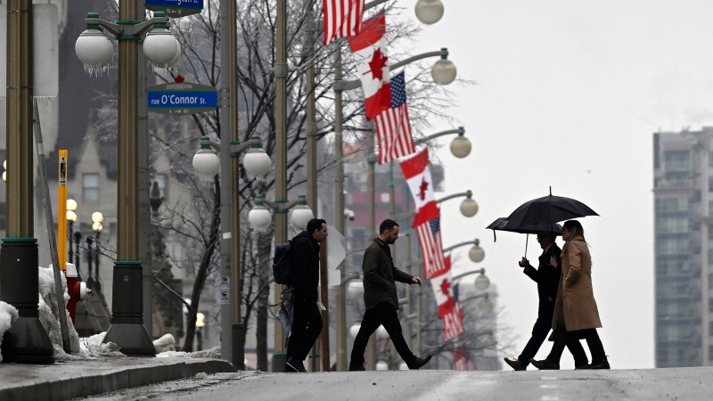 People hold umbrellas as they pass Canadian and American flags lining Wellington Street in front of Parliament Hill in Ottawa, before the visit of U.S. President Joe Biden to Canada, on Thursday, March 23, 2023. THE CANADIAN PRESS/Justin Tang