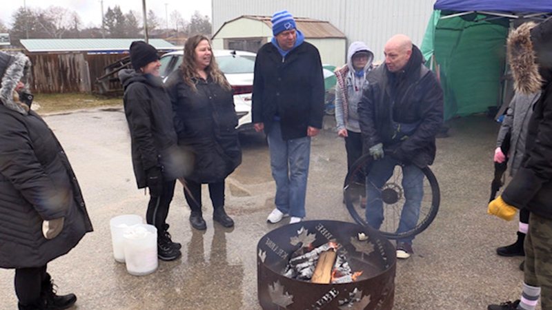 “This is Home 24-Hour Sleep Out” participants can be seen huddled around a bonfire outside of the thrift store It Takes a Village in Listowel, Ont. on March 25, 2023. (Scott Miller/CTV News London)