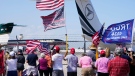 Supporters wave flags as they watch former U.S. President Donald Trump's plane depart Palm Beach International Airport in West Palm Beach, Fla., Saturday, March 25, 2023. Trump is traveling to Waco, Texas for a campaign rally. (AP Photo/Gerald Herbert)