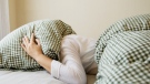 This stock photo shows a woman hiding her head under a pillow. (Credit: Shutterstock)