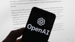 The OpenAI logo is seen on a mobile phone in front of a computer screen displaying output from ChatGPT, Tuesday, March 21, 2023, in Boston. Are tech companies moving too fast in rolling out powerful artificial intelligence technology that could one day outsmart humans? That is the conclusion of a group of prominent computer scientists and other tech industry notables who are calling for a 6-month pause to consider the risks. Their petition published Wednesday, March 29, 2023, is a response to San Francisco startup OpenAI's recent release of GPT-4. (AP Photo/Michael Dwyer, File)